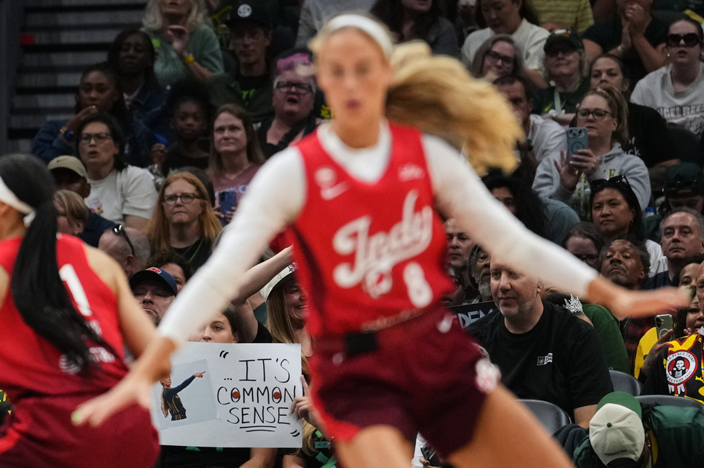 Indiana Fever guard Sophie Cunningham, front, runs by a fan holding a sign referencing her comments on transgender athletes and women's sports during the first half of a WNBA basketball game against the Seattle Storm, Tuesday, July 28, 2026, in Seattle. (AP Photo/Lindsey Wasson)