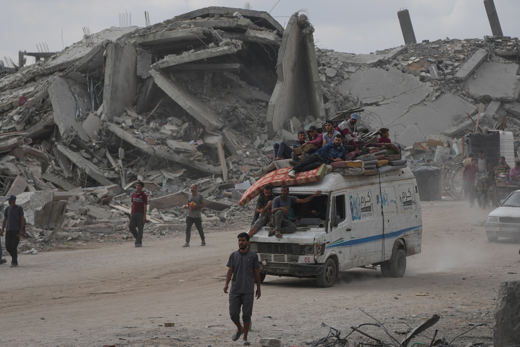 Displaced Palestinians ride on a van loaded with their belongings amid rubble in Gaza City, Sunday, Oct. 12, 2025, after Israel and Hamas agreed to a pause in their war and the release of the remaining hostages. (AP Photo/Abdel Kareem Hana)