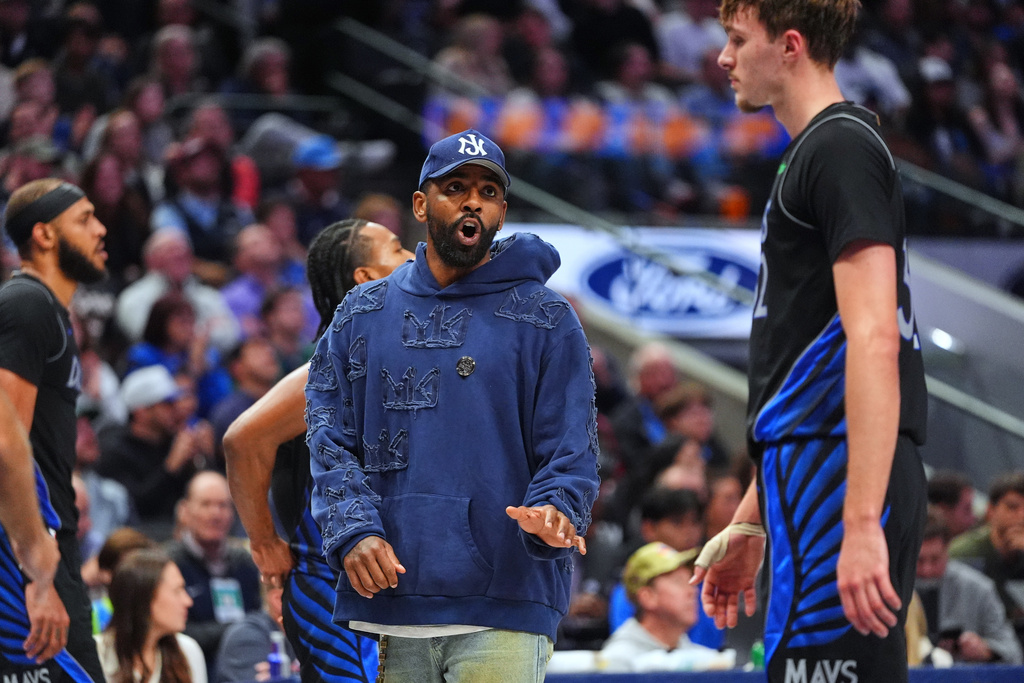 Injured Dallas Mavericks guard Kyrie Irving, left, talks with forward Cooper Flagg, right, during a timeout in the second half of an NBA basketball game against the Memphis Grizzlies in Dallas, Saturday, Nov. 22, 2025. (AP Photo/LM Otero)