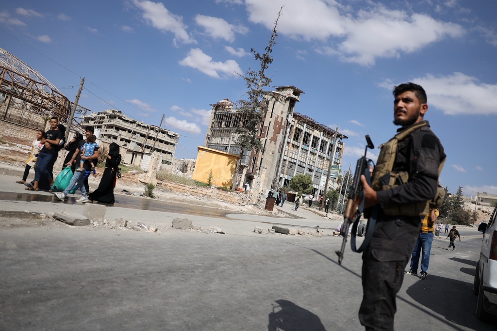 Syrian security forces stand guard as residents leave the Sheikh Maqsoud and Achrafieh neighborhoods of Aleppo, Syria, Tuesday, Oct. 7, 2025, following overnight clashes between Syrian government troops and the Kurdish-led Syrian Democratic Forces. (AP Photo/Omar Albam)