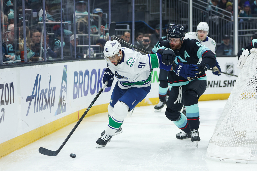 Vancouver Canucks left wing Evander Kane (91) moves the puck while defended by Seattle Kraken defenseman Adam Larsson (6) in the second period during an NHL hockey game Saturday, Feb. 28, 2026, in Seattle. (AP Photo/Kevin Ng)