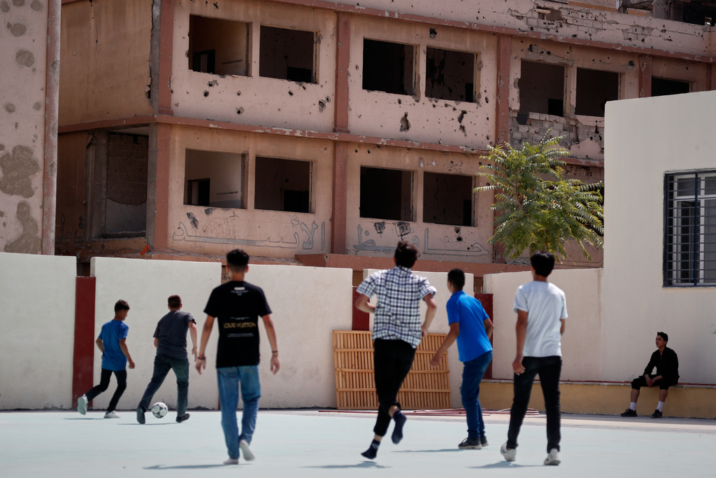 Students play soccer in the courtyard of a rehabilitated school, with a damaged building bearing graffiti praising former President Hafez Assad seen in the background, in the Damascus suburb of Douma, Syria, Thursday, Sept. 25, 2025. (AP Photo/Omar Sanadiki)