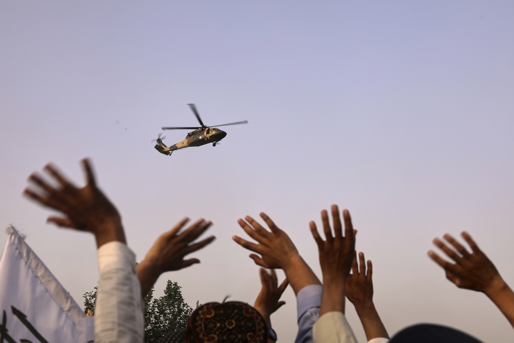 People wave to a military helicopter after it dropped flowers over the city during celebrations marking the fourth anniversary of the U.S. withdrawal and the start of Taliban rule in Kabul, Afghanistan, Friday, Aug. 15, 2025. (AP Photo/Siddiqullah Alizai)