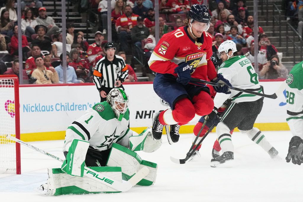 Florida Panthers left wing A.J. Greer (10) jumbos to avoid the puck as Dallas Stars goaltender Casey DeSmith (1) defends the goal during the second period of an NHL hockey game, Saturday, Nov. 1, 2025, in Sunrise, Fla. (AP Photo/Lynne Sladky)
