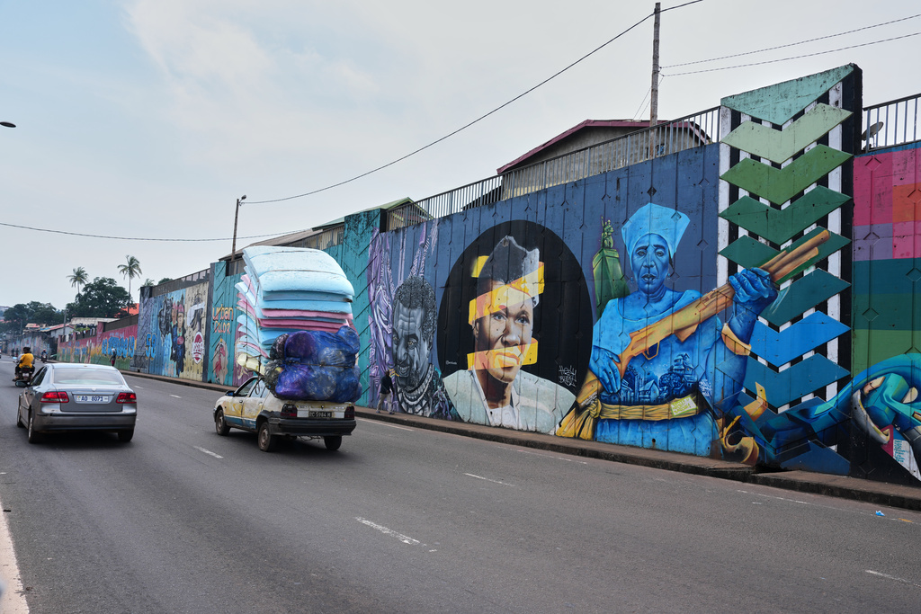 Cars drive past a long stretch of murals along a main road in Conakry, Guinea, Saturday, Sep. 20, 2025. (AP Photo/Misper Apawu)
