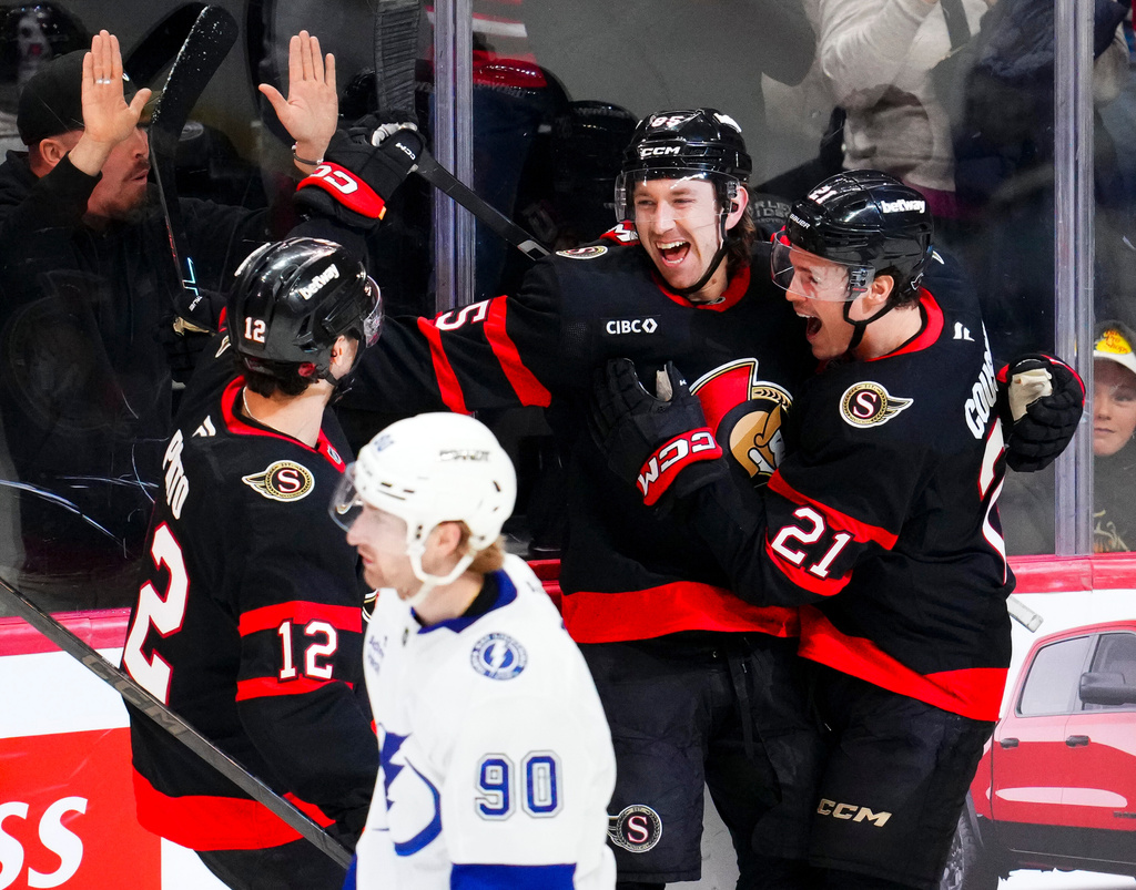 Ottawa Senators' Jake Sanderson, back center, celebrates his goal with teammates Shane Pinto (12), and Nick Cousins (21) as Tampa Bay Lightning's J.J. Moser (90) skates past during the third period of an NHL hockey game in Ottawa, Ontario, on Tuesday, April 7, 2026. (Sean Kilpatrick/The Canadian Press via AP)