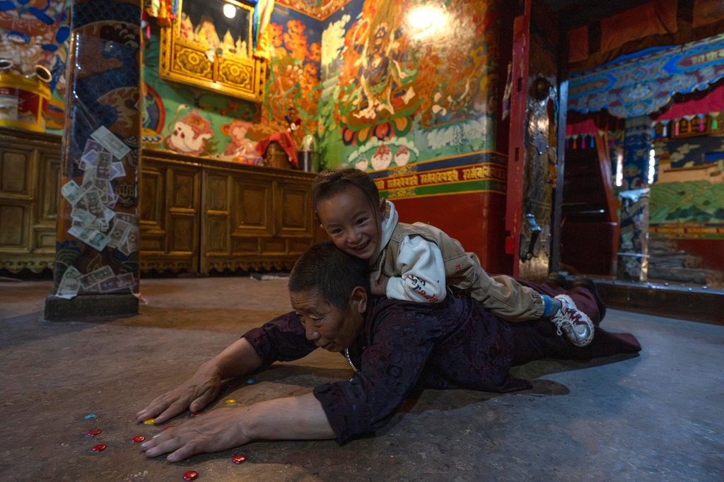 A child climbs onto a woman as she performs prostrations inside the monastery of the Yumbulagang Palace, regarded as Tibet's first palace, in Shannan in western China's Tibet Autonomous Region on Thursday, July 23, 2026, as seen during a government organized visit for foreign journalists. (AP Photo/Ng Han Guan)