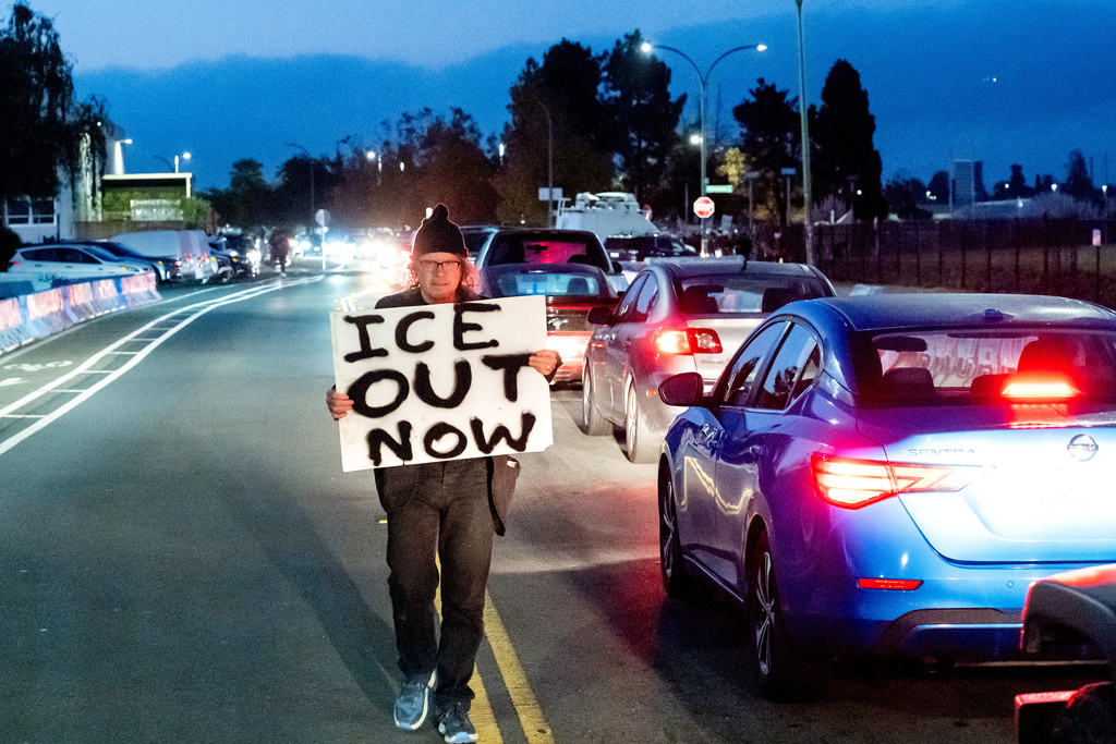 A protester holds a sign while fellow demonstrators block traffic to Coast Guard Base Alameda on Thursday, Oct. 23, 2025, in Oakland, Calif. (AP Photo/Noah Berger)