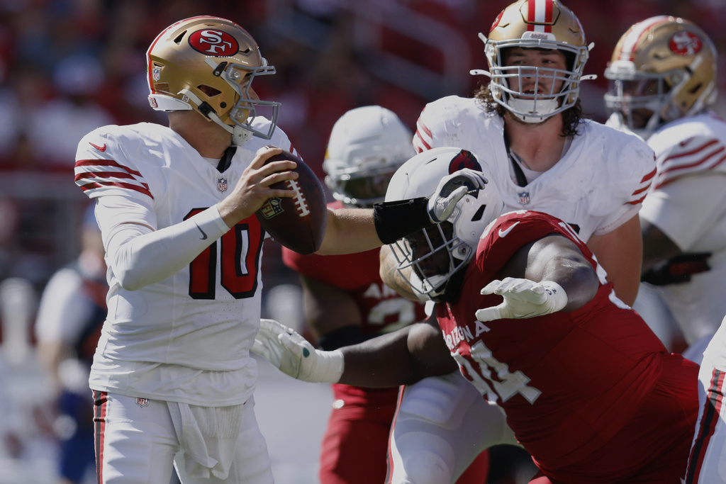 San Francisco 49ers quarterback Mac Jones, left, avoids a tackle by Arizona Cardinals defensive end Dalvin Tomlinson during the second half of an NFL football game Sunday, Sept. 21, 2025, in Santa Clara, Calif. (AP Photo/Sergio Estrada)
