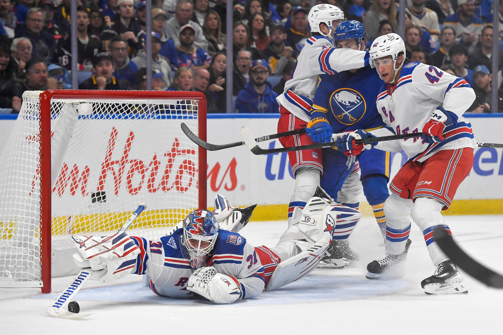 New York Rangers goalie Igor Shesterkin, left, reaches for a loose puck as defenseman Will Borgen, top left, and center Noah Laba, right, shield Buffalo Sabres left wing Jason Zucker during the second period of an NHL hockey game in Buffalo, N.Y., Thursday, Oct. 9, 2025. (AP Photo/Adrian Kraus)