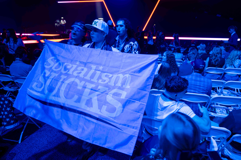 Students wave a flag reading "Socialism SUCKS" during Turning Point USA's AmericaFest 2025, Thursday, Dec. 18, 2025, in Phoenix. (AP Photo/Jon Cherry)