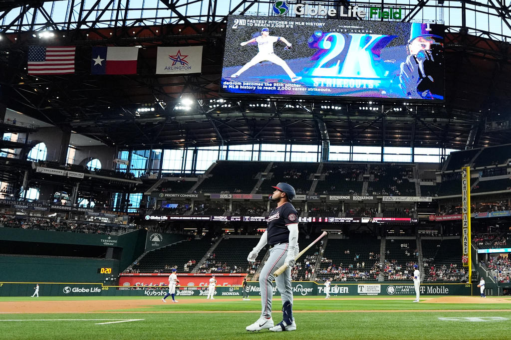 Washington Nationals designated hitter Abimelec Ortiz, center front, walks to the dugout after striking out against Texas Rangers pitcher Jacob deGrom, second from back right, which gave deGrom his 2,000th career strikeout, in the first inning of a baseball game Thursday, Aug. 20, 2026, in Arlington, Texas. (AP Photo/Tony Gutierrez)