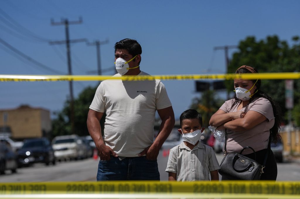 People wear masks while watching firefighters fight a warehouse fire in the Boyle Heights neighborhood of Los Angeles, Sunday, June 21, 2026. (AP Photo/Jae C. Hong)