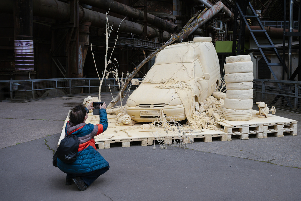 A woman takes a photo of the installation "Les Silence des Departs" by artist Tomas Lacque at the exhibition Urban Art Biennale 2026 at the former ironworks Voelklinger Huette, World Cultural Heritage Site, in Voelklingen, Germany, Wednesday, May 6, 2026. (Oliver Dietze/dpa via AP)