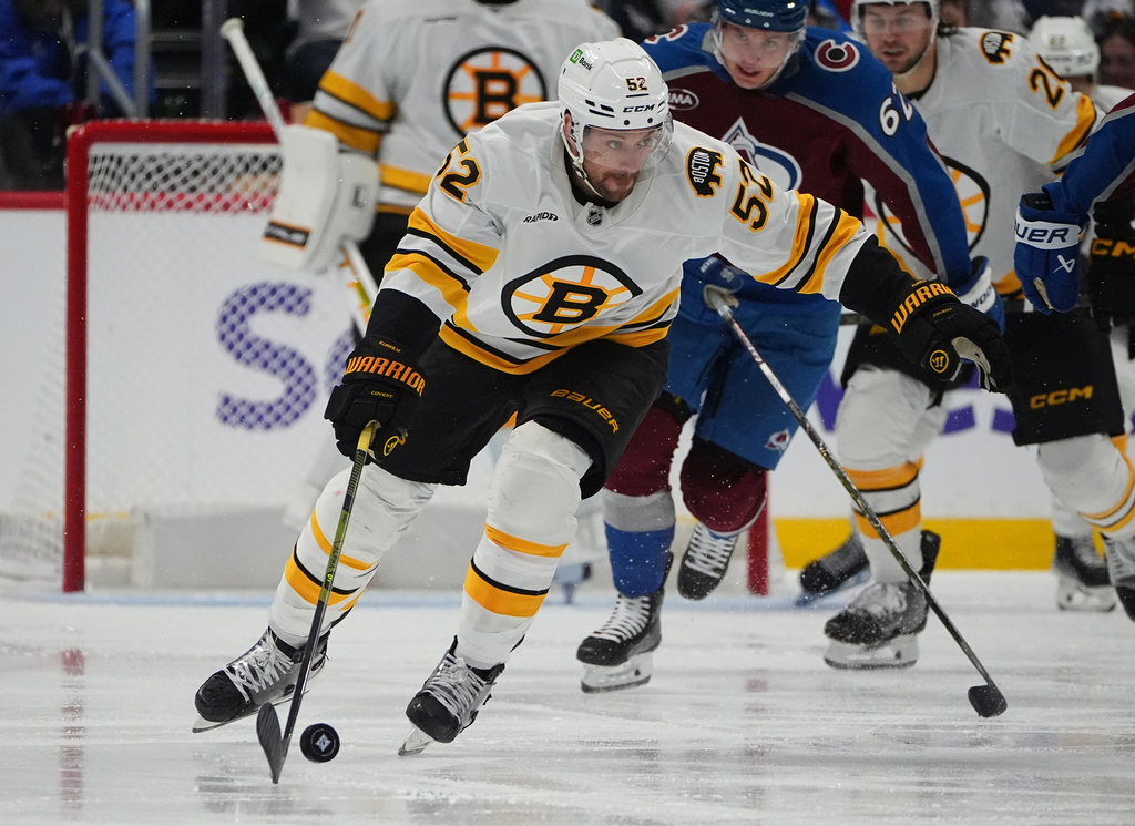 Boston Bruins center Sean Kuraly, front, collects the puck as Colorado Avalanche left wing Artturi Lehkonen (62) pursues in the second period of an NHL hockey game Saturday, Oct. 18, 2025, in Denver. (AP Photo/David Zalubowski)