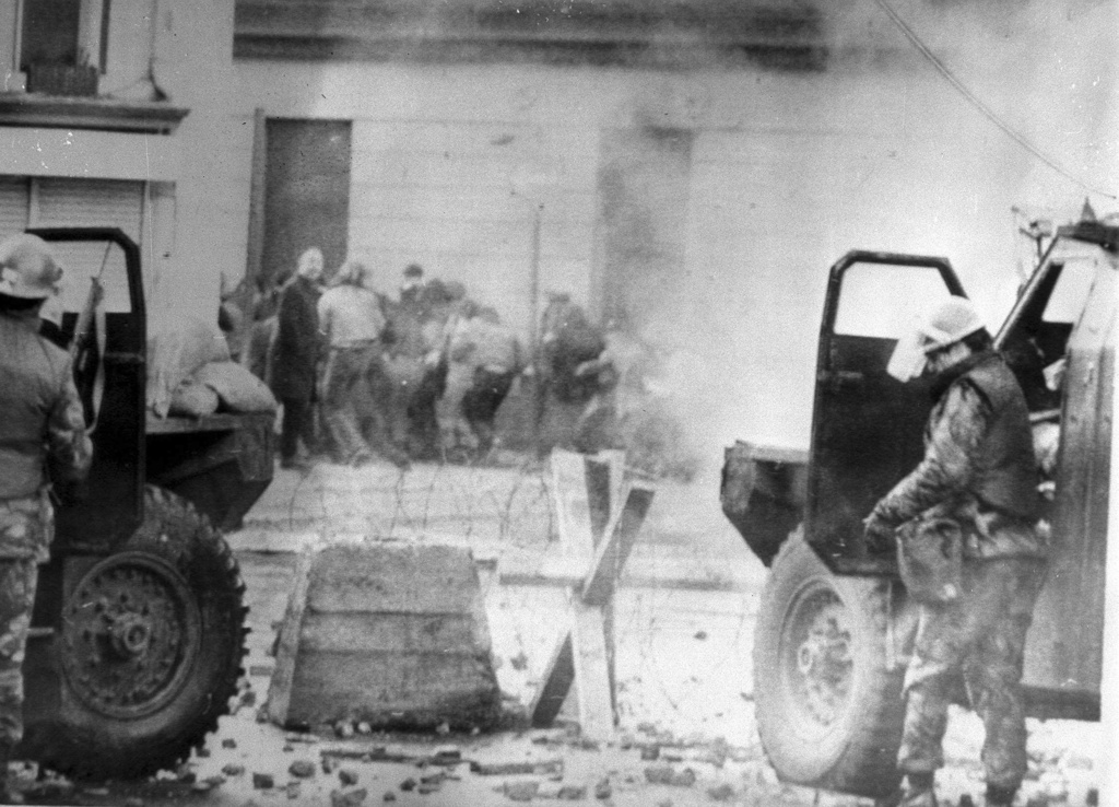Soldiers take cover behind their sandbagged armoured cars while dispersing rioters with CS gas in Londonderry, Northern Ireland, on Jan. 1, 1972. (PA via AP)