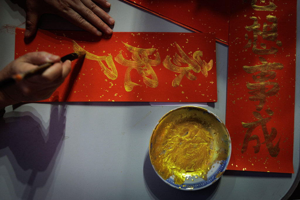 A woman brushes gold calligraphy onto red paper used for Lunar New Year couplets in Hong Kong, Feb. 11, 2026. (AP Photo/May James)
