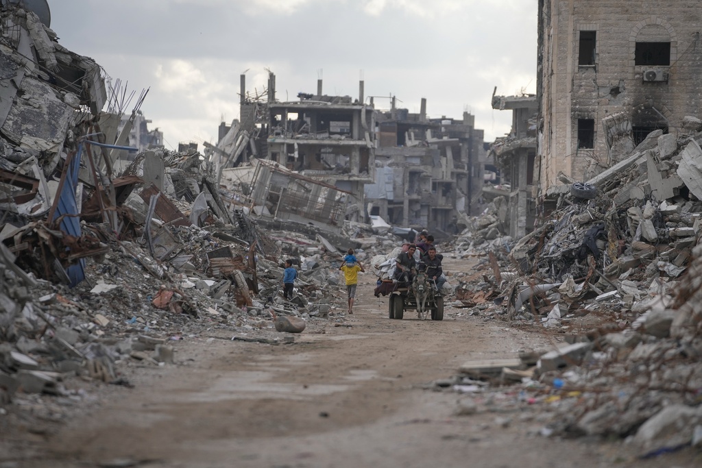 Palestinians move along a street flanked by the rubble of residential buildings destroyed in Israeli strikes in the Sheikh Radwan neighborhood of Gaza City, Friday, Nov. 14, 2025. (AP Photo/Jehad Alshrafi)