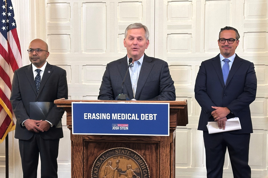 North Carolina Gov. Josh Stein, center, flanked by Health and Human Services Secretary Dr. Dev Sangvai, left, and Undue Medical Debt Vice Chair Jose Penabad, speaks about the elimination of medical debt through an initiative involving hospitals and Medicaid at the Executive Mansion in Raleigh, N.C., Monday, Oct. 13, 2025. (AP Photo/Gary D. Robertson)