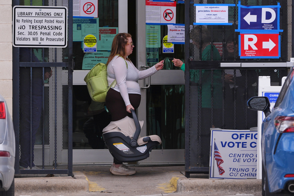 Primary voter Allie Davis carries her seven-week-old son Declan as a Dallas County Election Navigator checks her ID before entering a voting center in Dallas, Tuesday, March 3, 2026. (AP Photo/LM Otero)