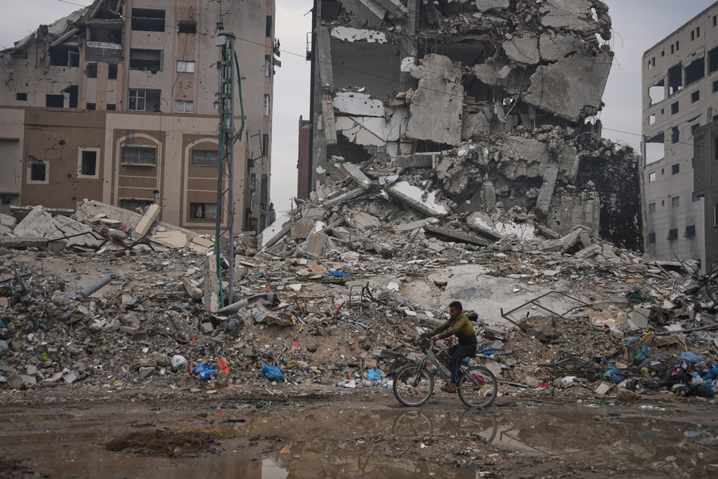 A Palestinian man rides a bicycle past destroyed buildings in Gaza City Sunday, Jan. 4, 2026. (AP Photo/Jehad Alshrafi)