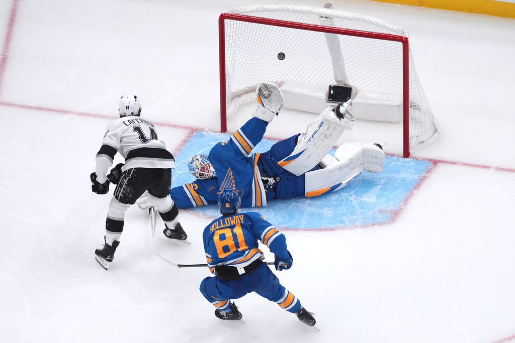 Los Angeles Kings' Alex Laferriere (14) scores past St. Louis Blues goaltender Jordan Binnington (50) as Blues' Dylan Holloway (81) watches during the second period of an NHL hockey game Tuesday, Oct. 21, 2025, in St. Louis. (AP Photo/Jeff Roberson)