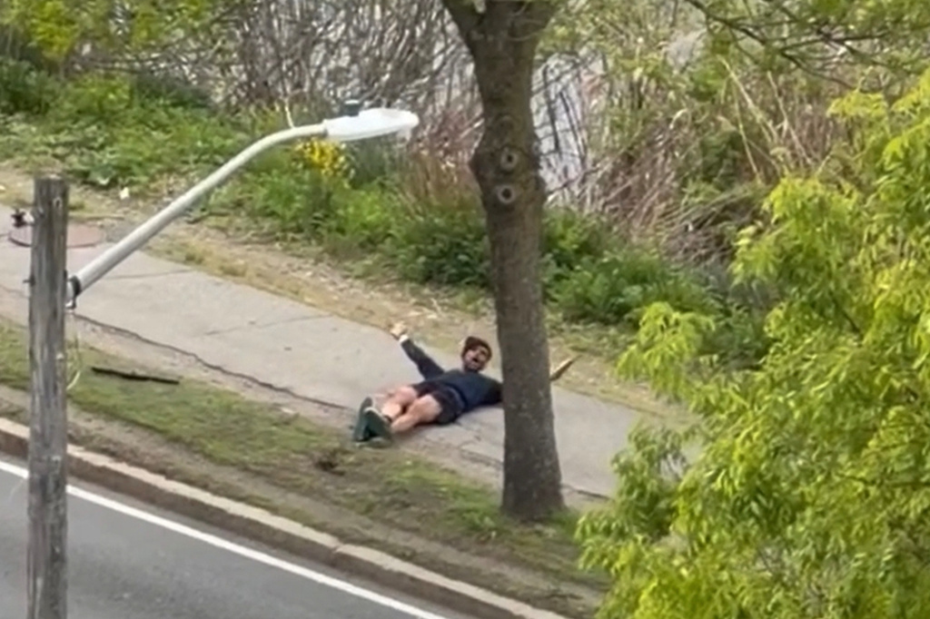 This image taken from video provided by Youssef Adel, shows a man with an assault-style rifle laid down on the ground after firing his weapons at a busy road outside in Cambridge, Mass. on Monday, May 11, 2026. (Youssef Adel via AP)