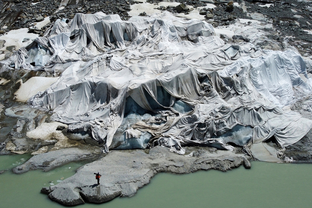 FILE — The Rhone Glacier near Goms, Switzerland, is partially covered with sheets as Matthias Huss, head of the Swiss glacier monitoring group GLAMOS, stands nearby, on June 10, 2025. (AP Photo/Matthias Schrader, File)