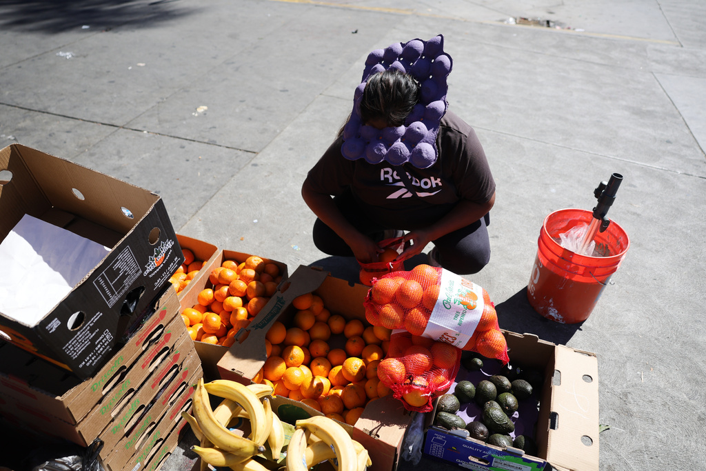 A street vendor uses an egg carton to shield from from during an unseasonably hot day at MacArthur Park on Thursday, March 12, 2026, in Los Angeles. (AP Photo/Ryan Sun)