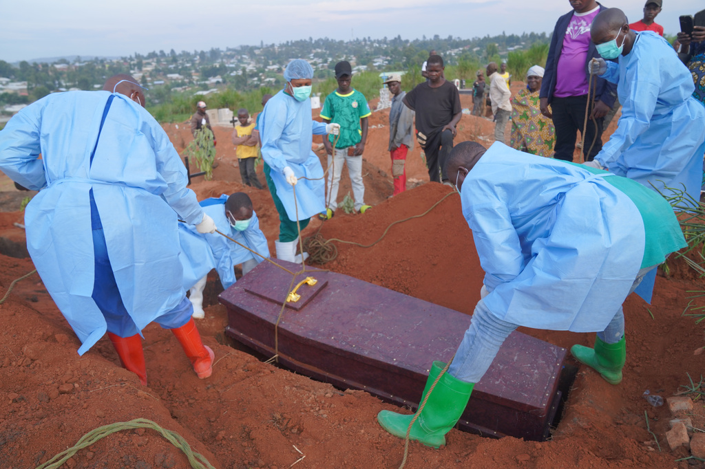 People dressed in protective gear lower into a grave the coffin containing the remains of 6-year-old Baudjo Baraka Jules, who died of Ebola, in Bunia, Ituri province, eastern Congo, Tuesday, Aug. 18, 2026. (AP Photo/Dieudonne Dirole)
