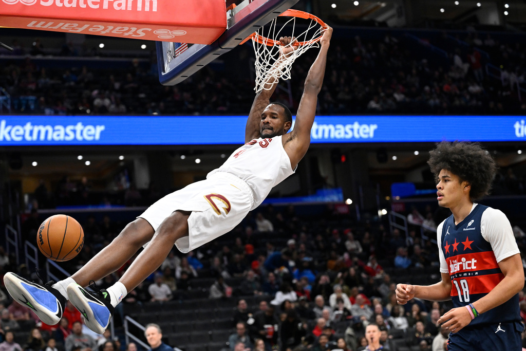 Cleveland Cavaliers center Evan Mobley, left, hangs from the rim after dunking against Washington Wizards forward Kyshawn George, right, during the first half of an NBA basketball game Friday, Dec. 12, 2025, in Washington. (AP Photo/John McDonnell)