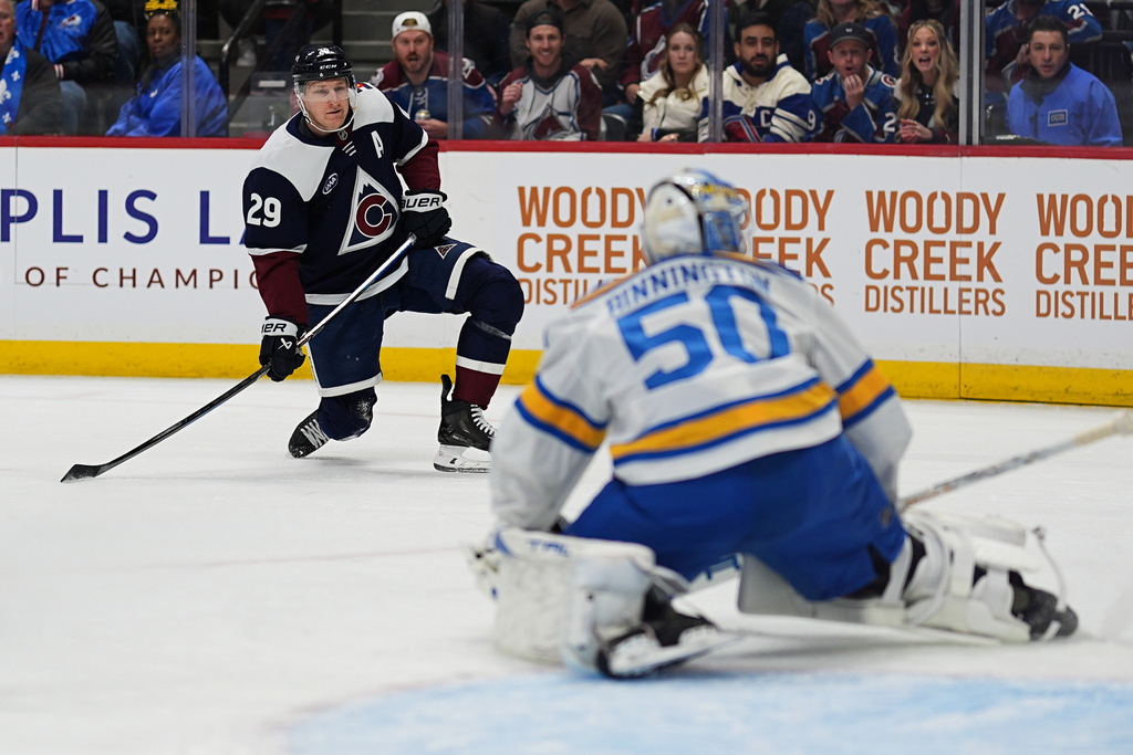 Colorado Avalanche center Nathan MacKinnon, back, shoots the puck at St. Louis Blues goaltender Jordan Binnington in the first period of an NHL hockey game, Wednesday, Dec. 31, 2025, in Denver. (AP Photo/David Zalubowski)