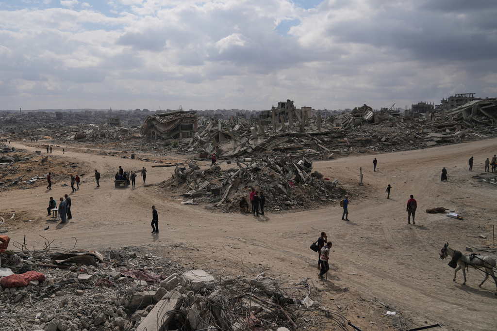 Displaced Palestinians walk amid destroyed buildings in Al-Jalaa Street in Gaza City, Sunday, Oct. 12, 2025, after Israel and Hamas agreed to a pause in their war and the release of the remaining hostages. (AP Photo/Abdel Kareem Hana)