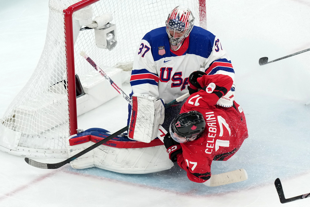 Canada's Macklin Celebrini (17) slides into United States goalkeeper Connor Hellebuyck (37) during the third period of the men's ice hockey gold medal game at the 2026 Winter Olympics in Milan, Italy, Sunday, Feb. 22, 2026. (AP Photo/Carolyn Kaster)