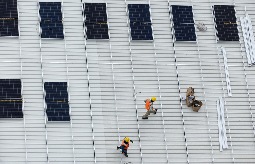 A pair of workers walk past recently installed solar panels on the roof of a warehouse near Jurong Island in Singapore on Oct. 6, 2025. (AP Photo/Anton L. Delgado)