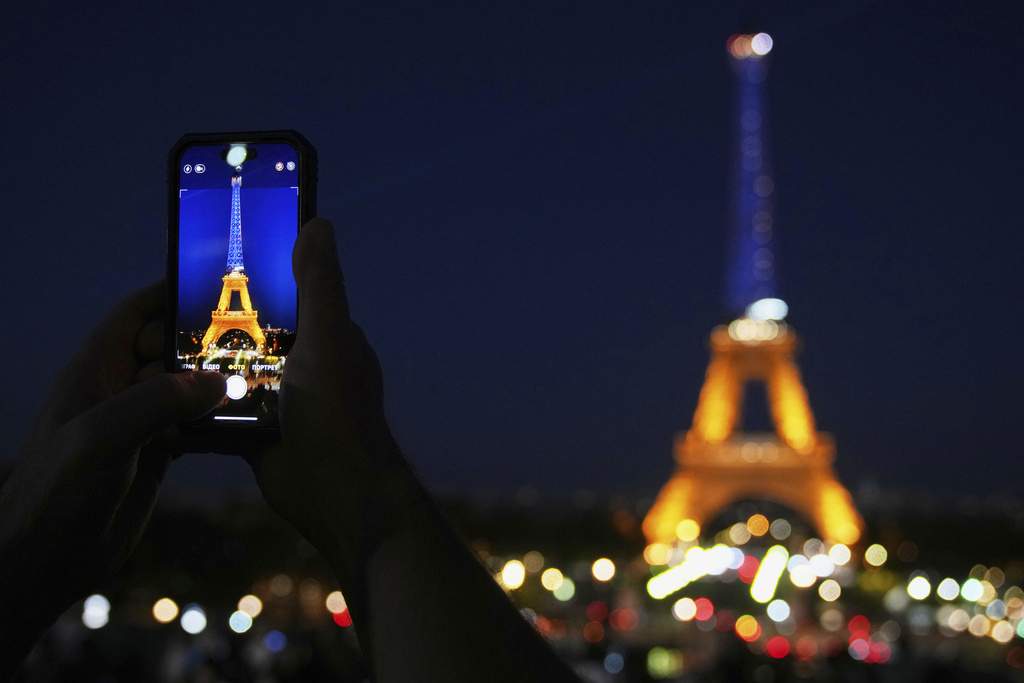 A man takes a photo of the Eiffel Tower illuminated with the colours of Ukraine in honor of it's Independence Day, in Paris, Sunday, Aug. 24, 2025. (AP Photo/Christophe Ena)