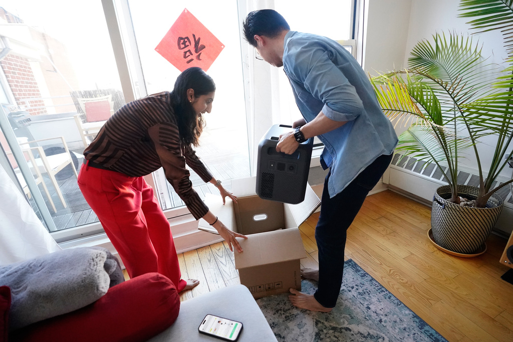 Sonam Velani and Yan Sim plug unbox a battery from Every Electric to power an air conditioner as part of a pilot program with the city's energy company Con Edison to reduce pressure on the electrical grid Monday, April 27, 2026, in the Brooklyn borough of New York. (AP Photo/Alyssa Goodman)