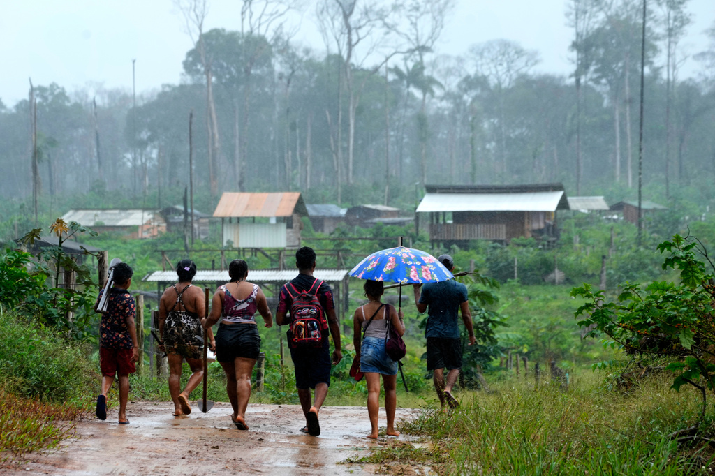 A family walks carrying tools toward an area known as Nova Conquista or New Conquest where families are building houses near the center of Oiapoque, Amapa state, Brazil, Tuesday, March 10, 2026. (AP Photo/Eraldo Peres)