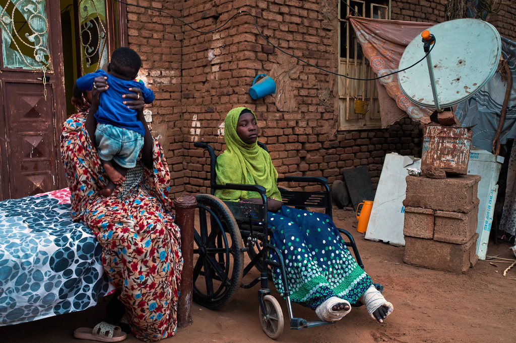 Noon Madani, 18, center, who was injured in a shelling attack, sits in a wheelchair on the patio of her family home in Khartoum, Monday, April 27, 2026. (AP Photo/Bernat Armangue)