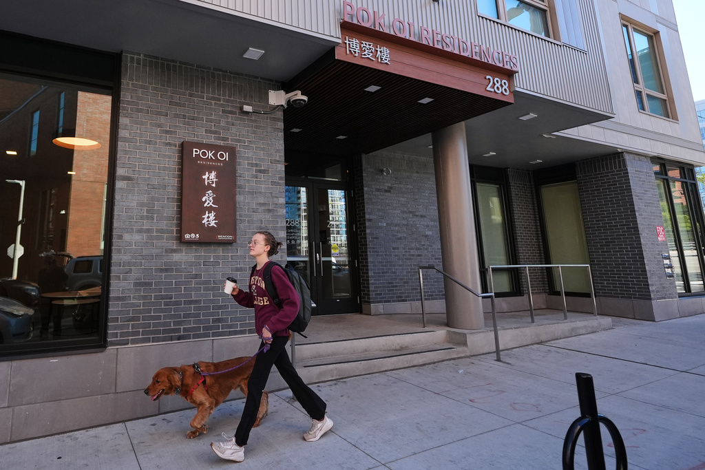 A woman walks her dog past the Pok Oi Residences, Oct. 17, 2025, in the Chinatown neighborhood of Boston. (AP Photo/Charles Krupa)