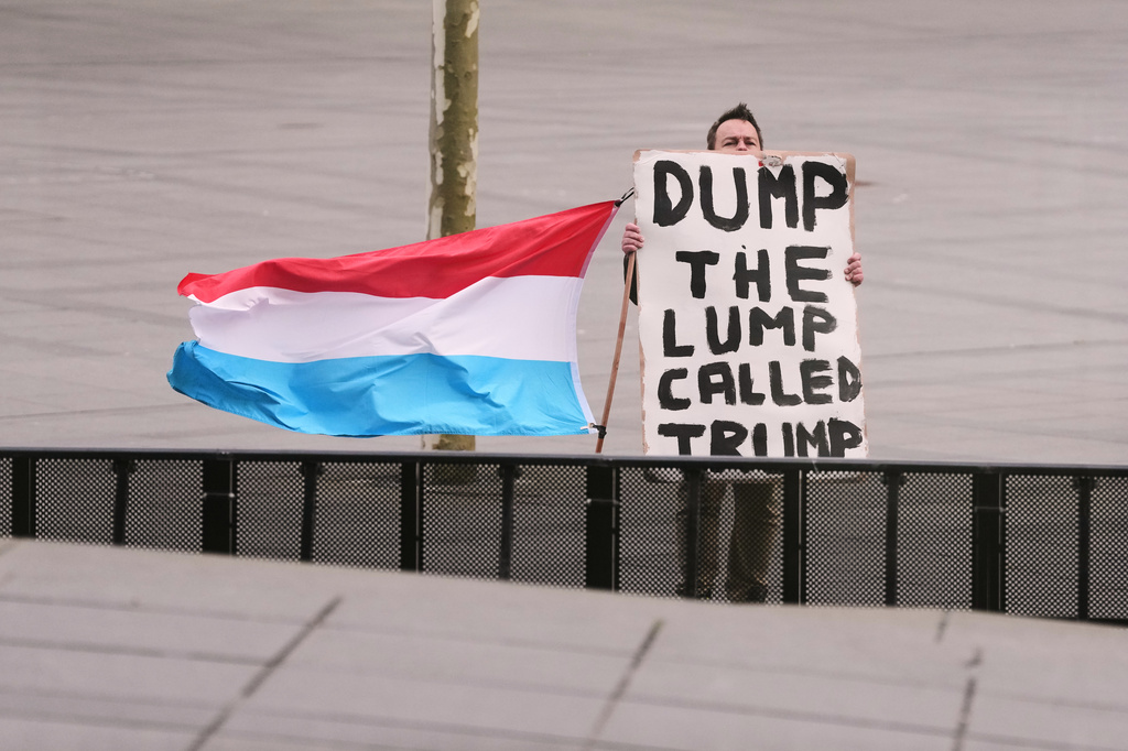 A man holds the flag of Luxembourg and a placard as he demonstrates outside a meeting of EU foreign ministers at the European Council building in Luxembourg, Tuesday, April 21, 2026. (AP Photo/Virginia Mayo)