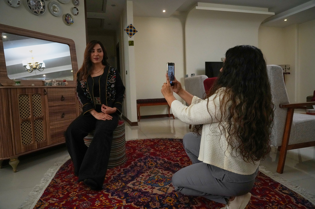Fashion designer Amen Khademi takes a photo with her cellphone of model Farnaz Ojaghloo wearing a jacket she designed with Persian-inspired motifs at her studio in Tehran, Iran, Thursday, April 23, 2026. (AP Photo/Vahid Salemi)