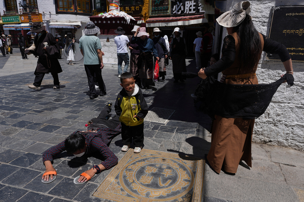 A child stands near a pilgrim performing full body prostrations along Barkhor Street in Lhasa in western China's Tibet Autonomous Region on Tuesday, July 21, 2026, as seen during a government organized visit for foreign journalists. (AP Photo/Ng Han Guan)
