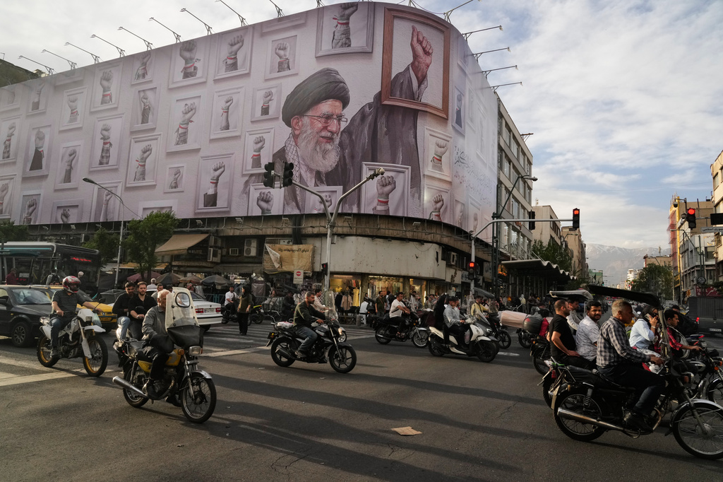 Motorbikes drive past a billboard with graphic showing the late Iranian Supreme Leader Ayatollah Ali Khamenei, who was killed in the U.S. and Israel strikes on Feb. 28, with his framed fist amongst his supporters framed fists in downtown Tehran, Iran, Wednesday, May 6, 2026. (AP Photo/Vahid Salemi)