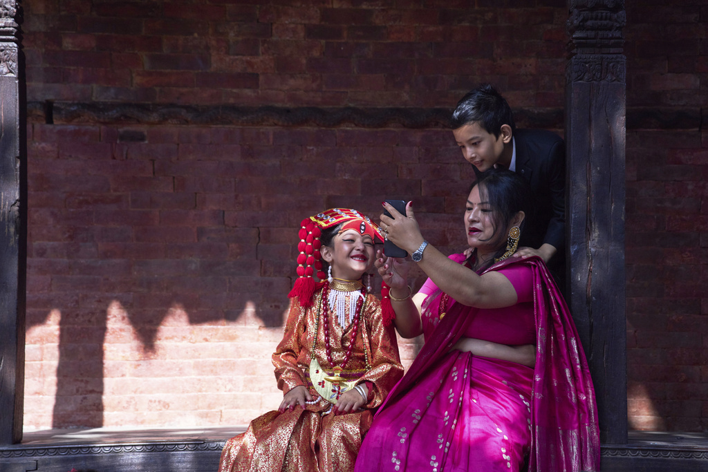 A Newar woman takes a selfie with her young daughter, dressed to represent divine female energy, and her son as they wait for Kumari Puja, a ritual during which the young girl would be worshipped, at Hanuman Dhoka, Basantapur Durbar Square, Kathmandu, Nepal, Friday, Sept. 5, 2025. (AP Photo/Niranjan Shrestha)
