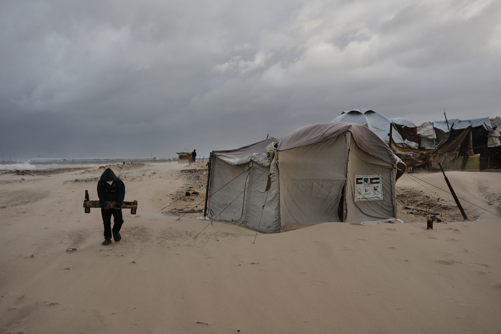 A man carries a piece of wood at a displacement camp sheltering Palestinians on a beach amid stormy weather in Gaza City, Tuesday, Jan. 13, 2026. (AP Photo/Jehad Alshrafi)