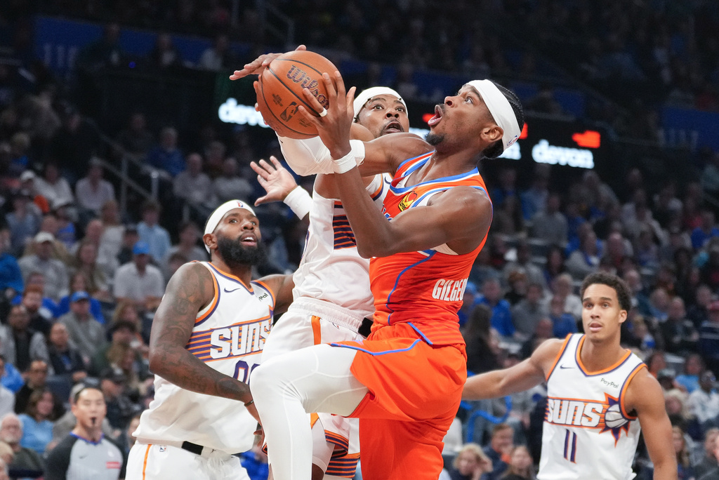 Oklahoma City Thunder guard Shai Gilgeous-Alexander, center right, shoots around Phoenix Suns guard Jordan Goodwin, center left, during the second half of an NBA Cup basketball game, Friday, Nov. 28, 2025, in Oklahoma City. (AP Photo/Kyle Phillips)