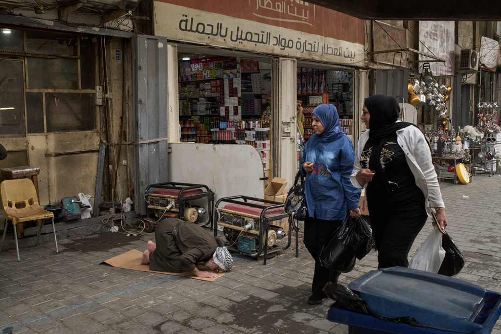Women walk past a man praying on the sidewalk in downtown of Baghdad, Iraq, Wednesday, March 25, 2026. (AP Photo/Leo Correa)