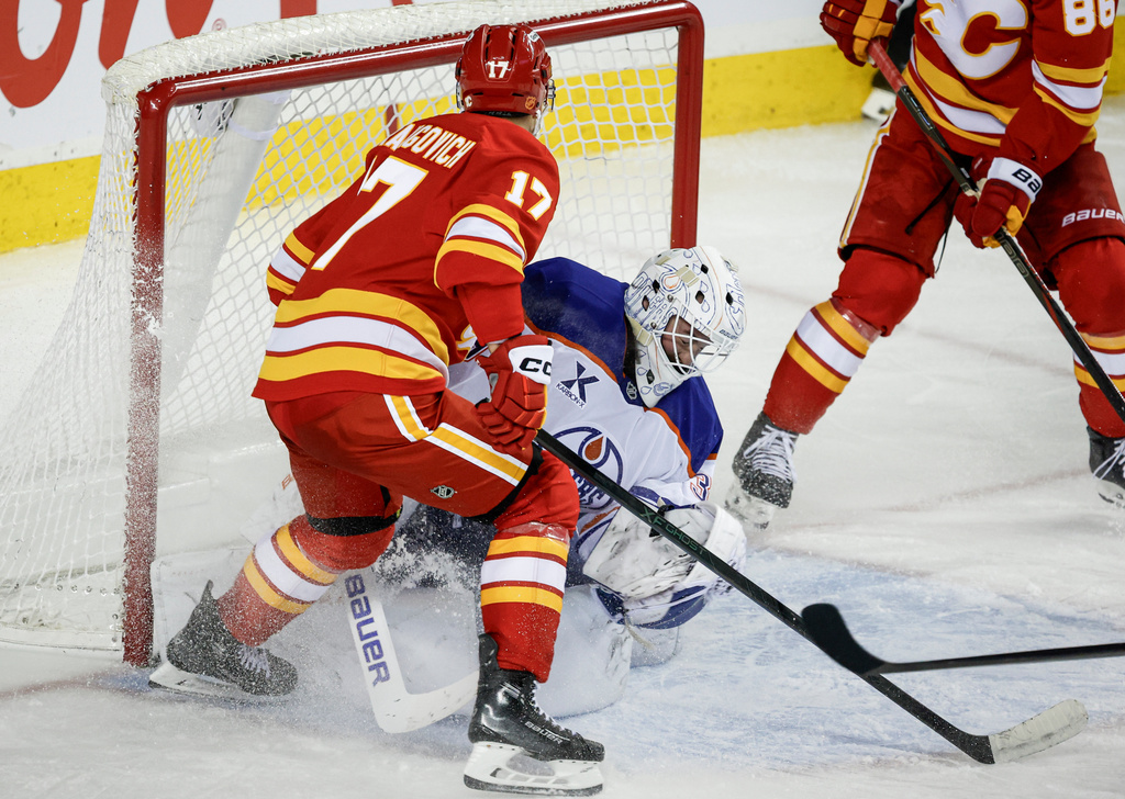 Edmonton Oilers goalie Connor Ingram, centeer, is knocked over by Calgary Flames' Yegor Sharangovich (17) during the third period of an NHL hockey game in Calgary, Alberta, Saturday, Dec. 27, 2025. (Jeff McIntosh/The Canadian Press via AP)