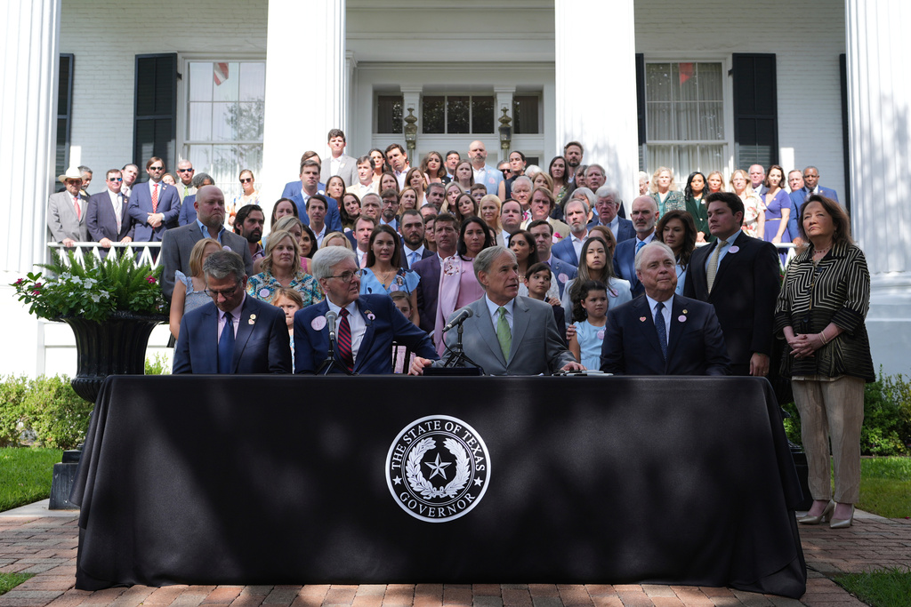 FILE - Parents and family of children who died at Camp Mystic join Texas Gov. Greg Abbott, second from right, as he signs camp safety bills, Sept. 5, 2025, in Austin, Texas. (AP Photo/Eric Gay, File